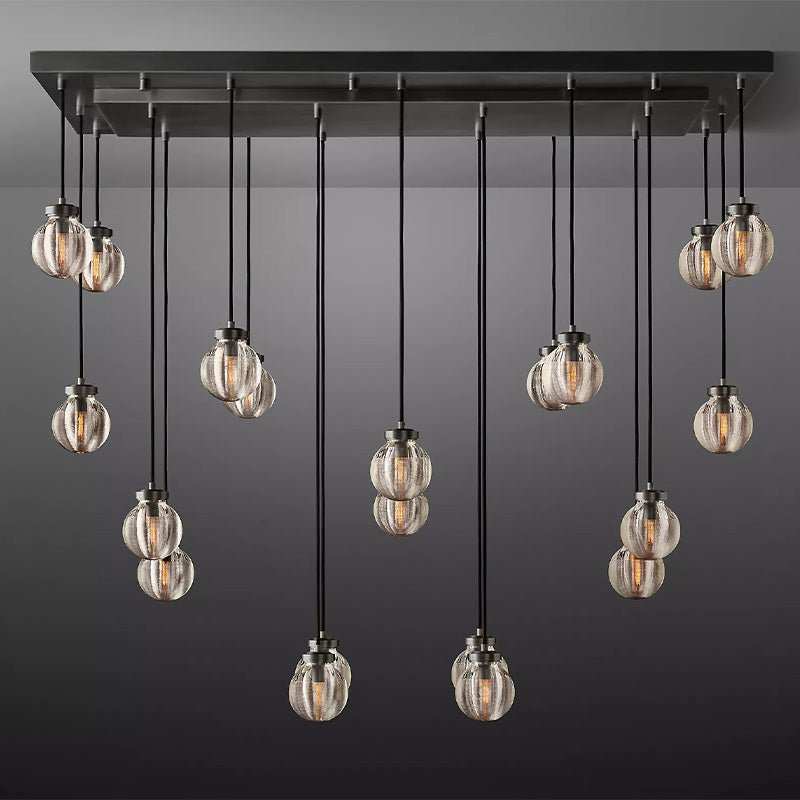 Linear chandelier with black metal frame and 12 ribbed glass globe pendants in warm amber tones, suspended against a gray background.